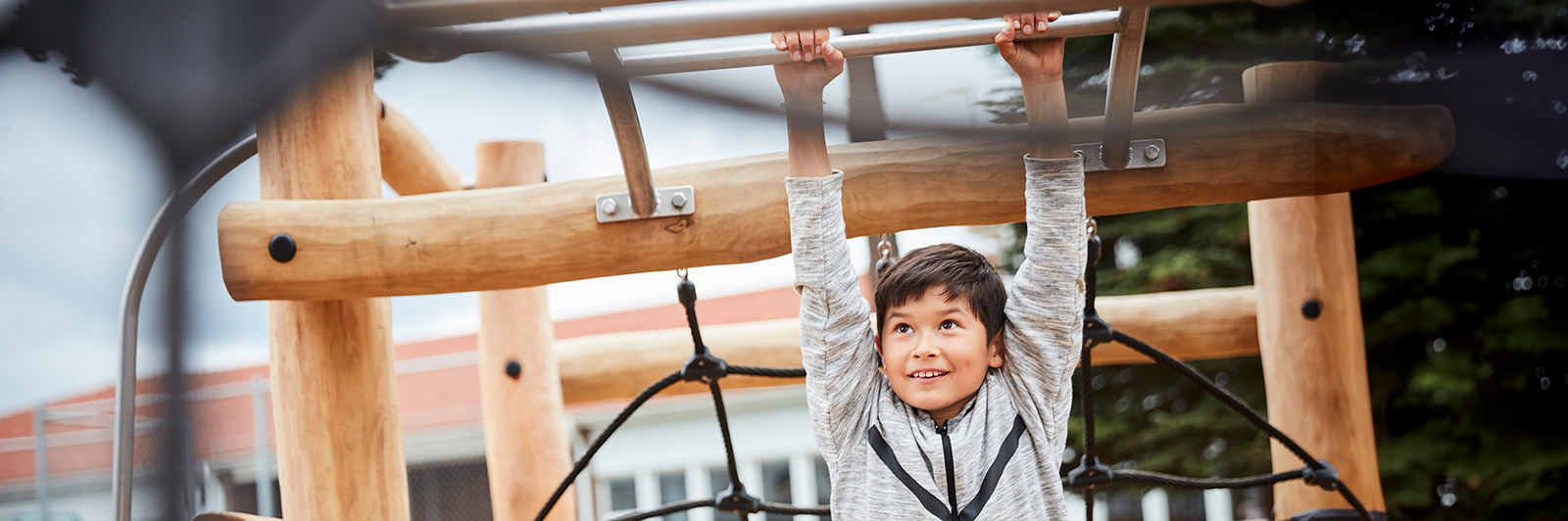 A boy hangs on monkey bars at a playground made out of robinia wood.